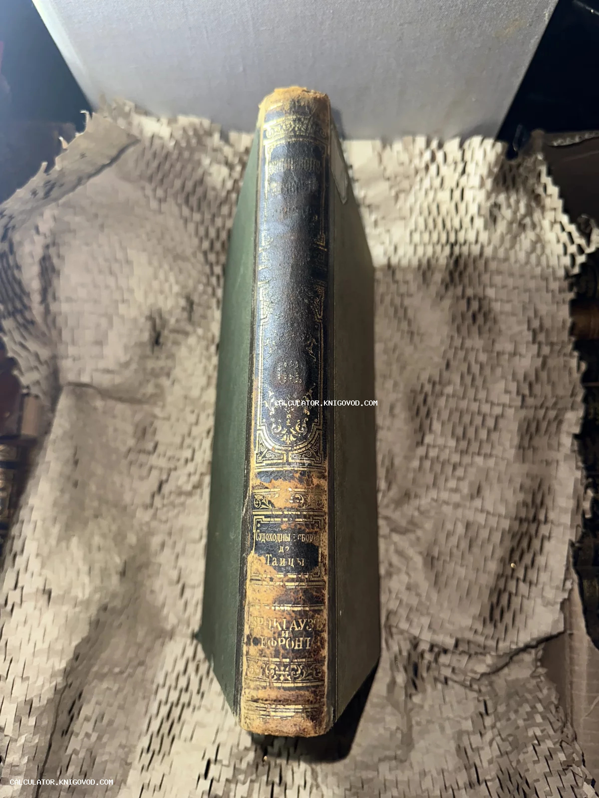 Корешок антикварной книги в полукожаном переплете с золотым тиснением на фоне упаковочного картона.