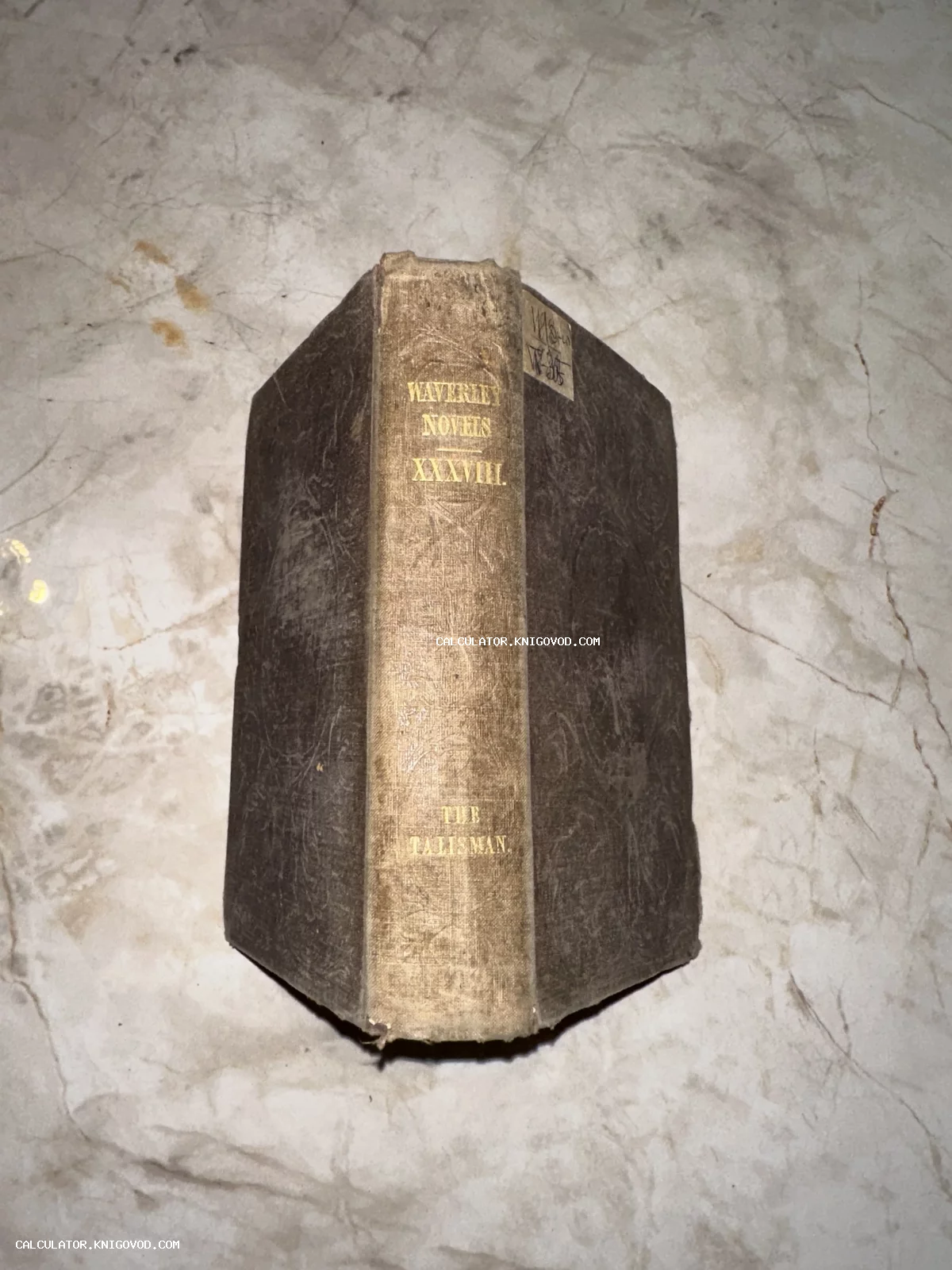 Старинная книга с золотым тиснением на корешке «Waverley Novels XXXVIII. The Talisman» на мраморной поверхности.
