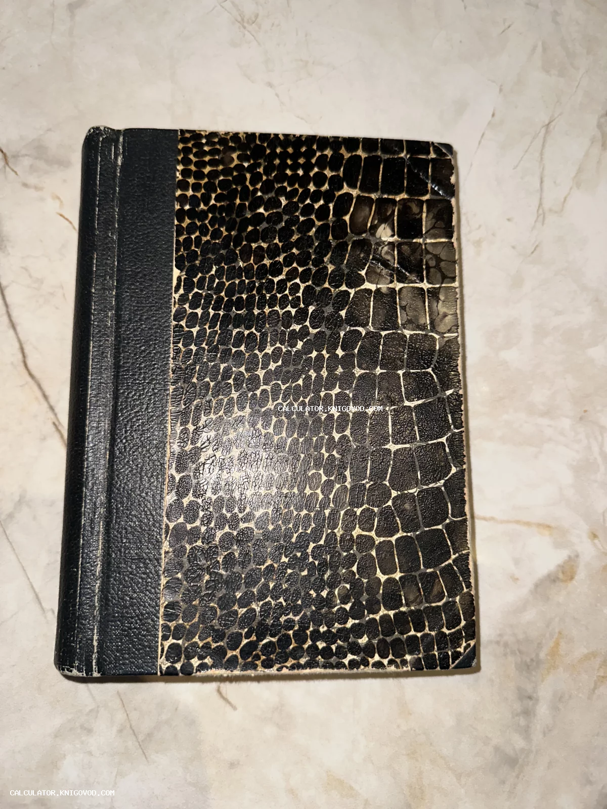 Старинная записная книжка с черным корешком и обложкой, имитирующей кожу крокодила или змеи, на мраморном фоне.