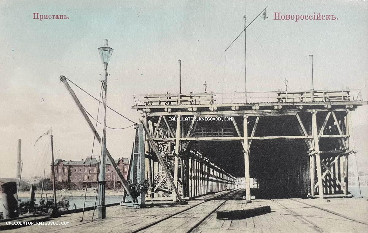 Черно-белая тонированная фотография деревянной пристани в Новороссийске с рельсами, портовыми кранами и фонарным столбом в начале XX века.