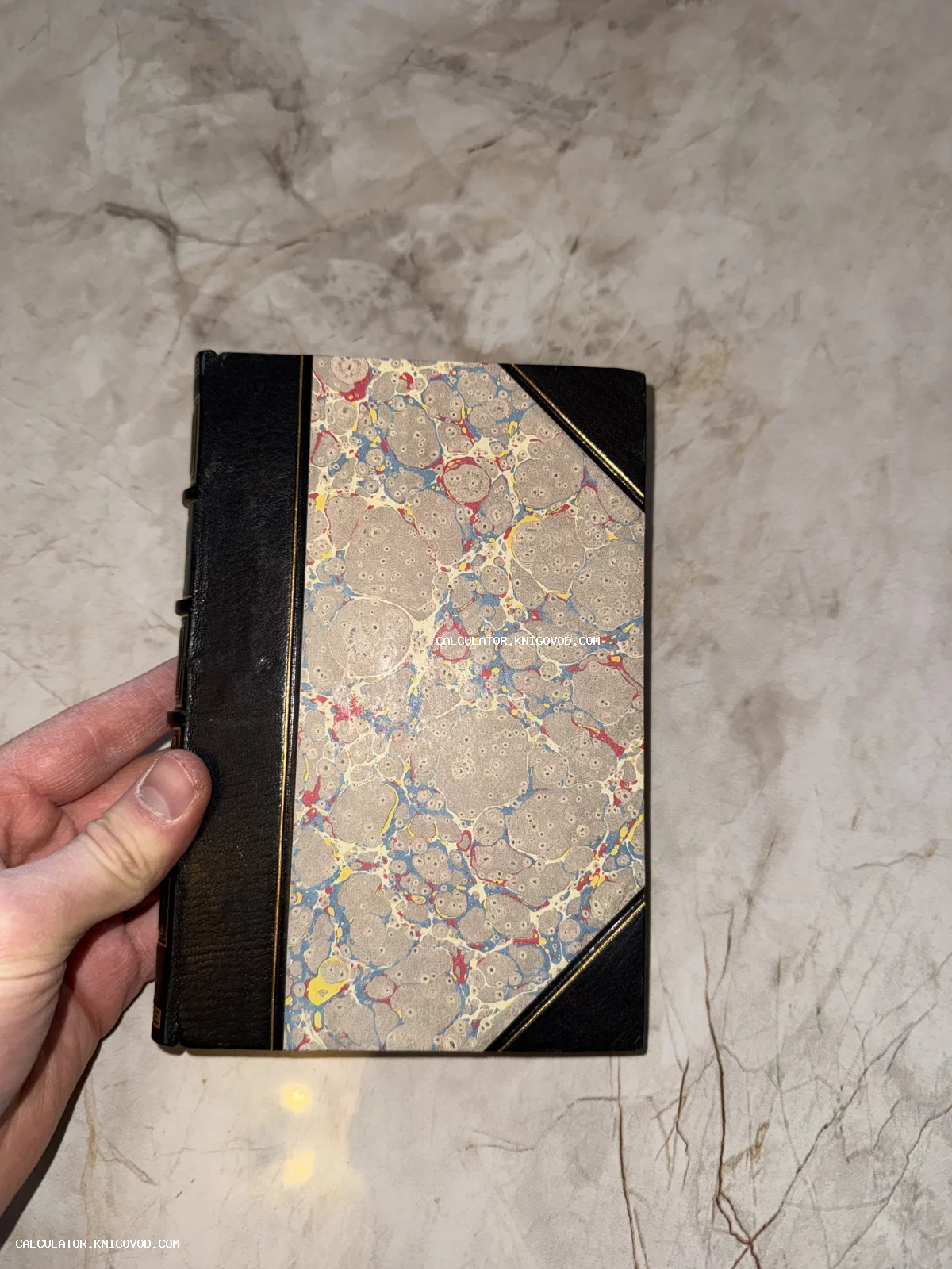 Старинная книга в черном полукожаном переплете с мраморной бумагой на обложке и золотым тиснением.