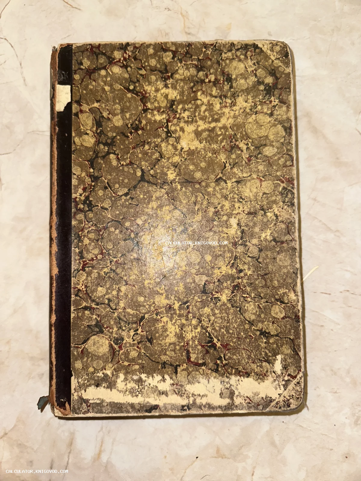Лицевая сторона обложки антикварной книги с узором мраморной бумаги и потертым темным корешком.