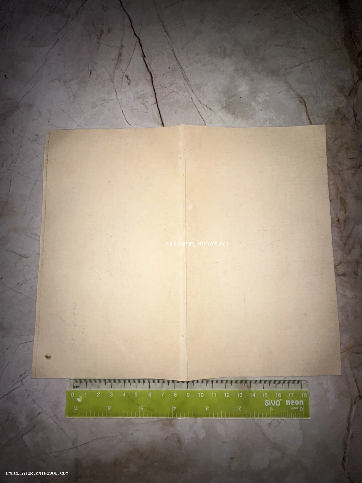 Старинный пожелтевший лист бумаги в развороте с линейкой для масштаба на мраморной поверхности.