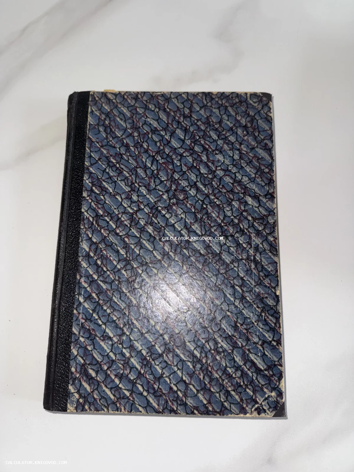 Старинная книга с сине-фиолетовым мраморным узором на обложке и черным корешком на светлом фоне.