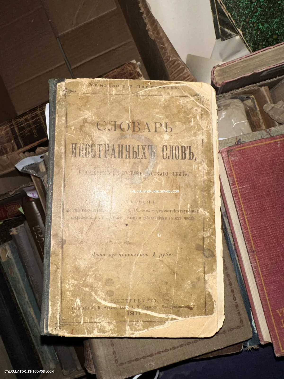 Старинная книга 'Словарь иностранных слов', изданная в Санкт-Петербурге в 1911 году, лежащая в стопке других антикварных изданий.