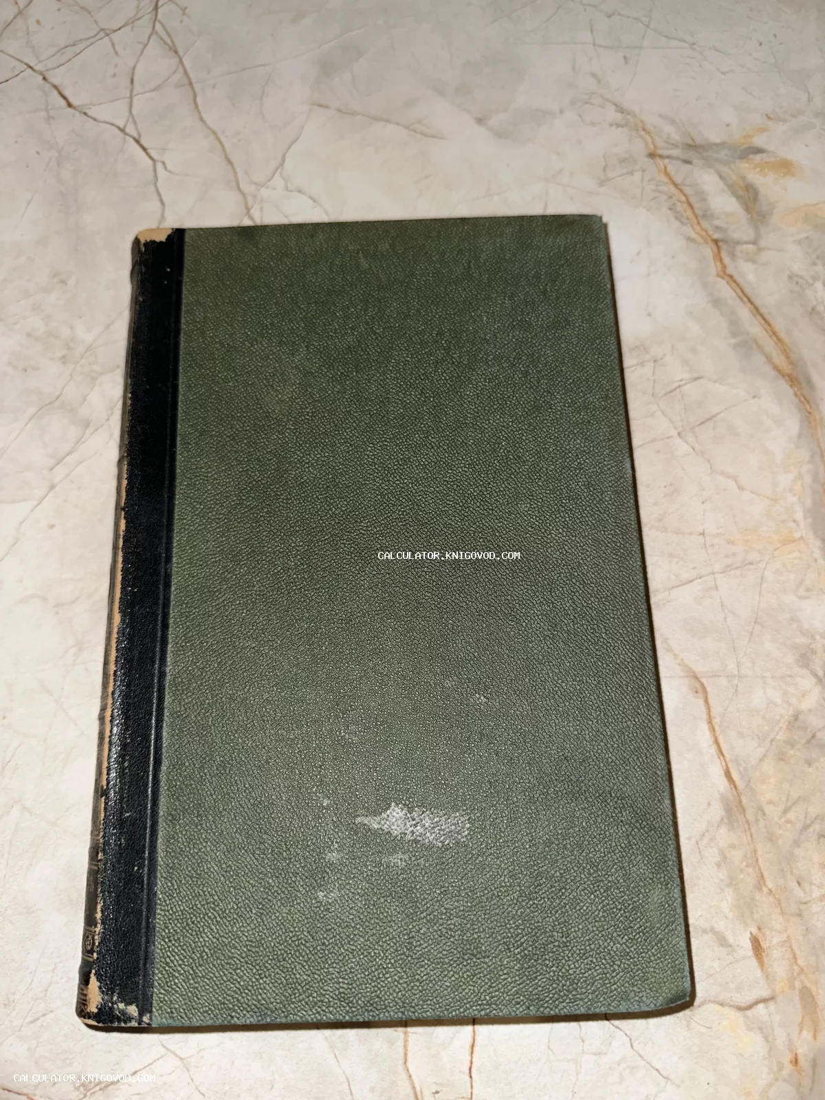 Старая книга в темно-зеленом твердом переплете с черным корешком, лежащая на мраморной поверхности.