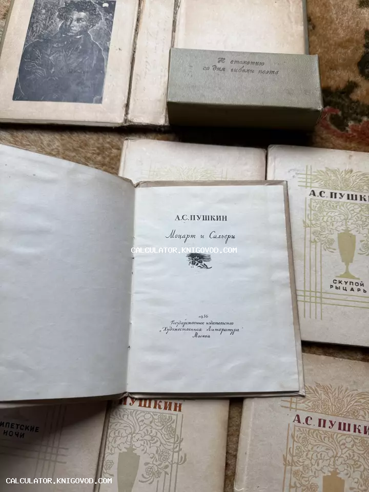 Раскрытая антикварная книга Пушкина «Моцарт и Сальери» на фоне портрета поэта и других томов серии в памятном футляре.