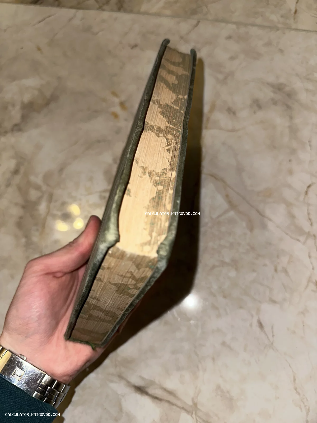 Вид сверху на обрез старой книги с крапчатым узором в руке человека на фоне мраморной поверхности.