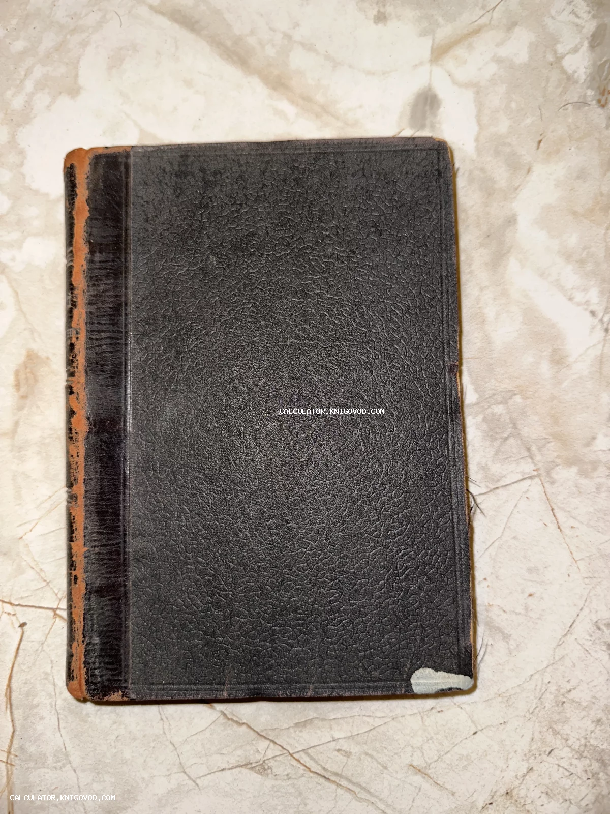 Старинная книга в черном фактурном переплете с потертым корешком на мраморном фоне