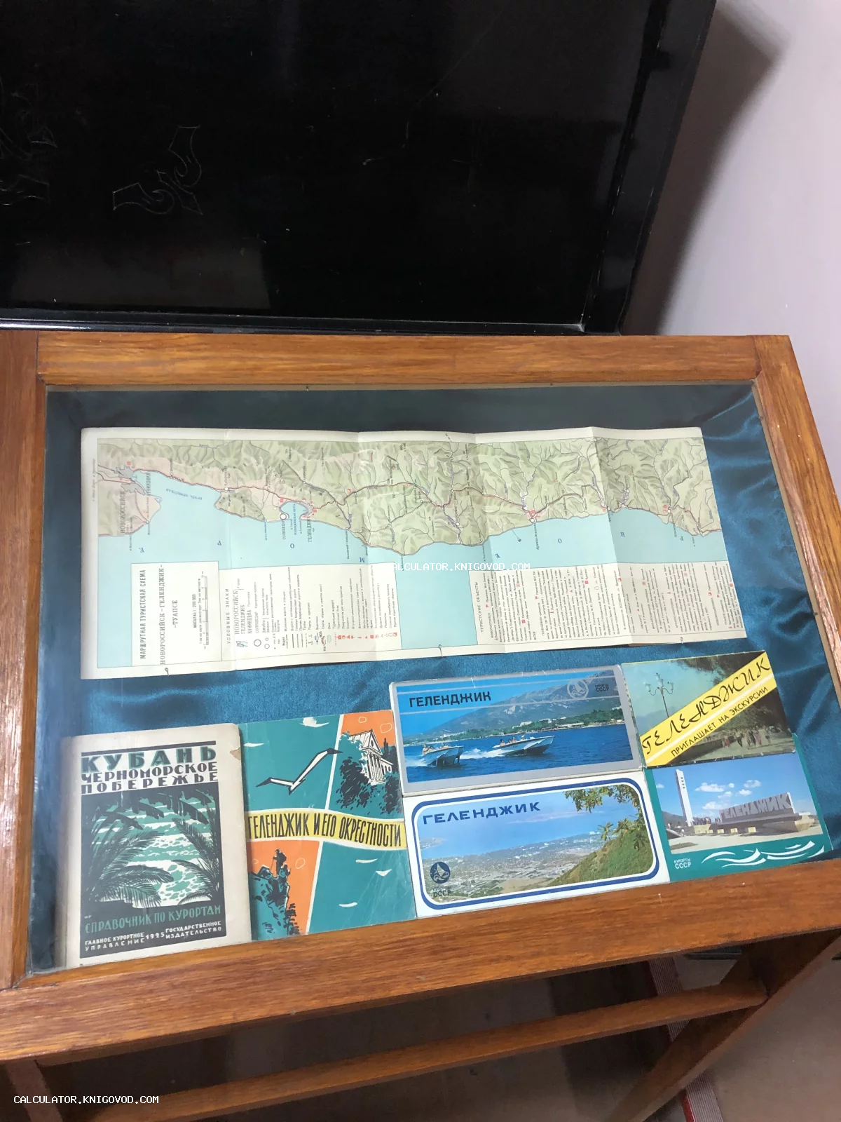 Старинная складная карта Новороссийска и Туапсе, справочник Кубань 1925 года и открытки Геленджика под стеклом в витрине.