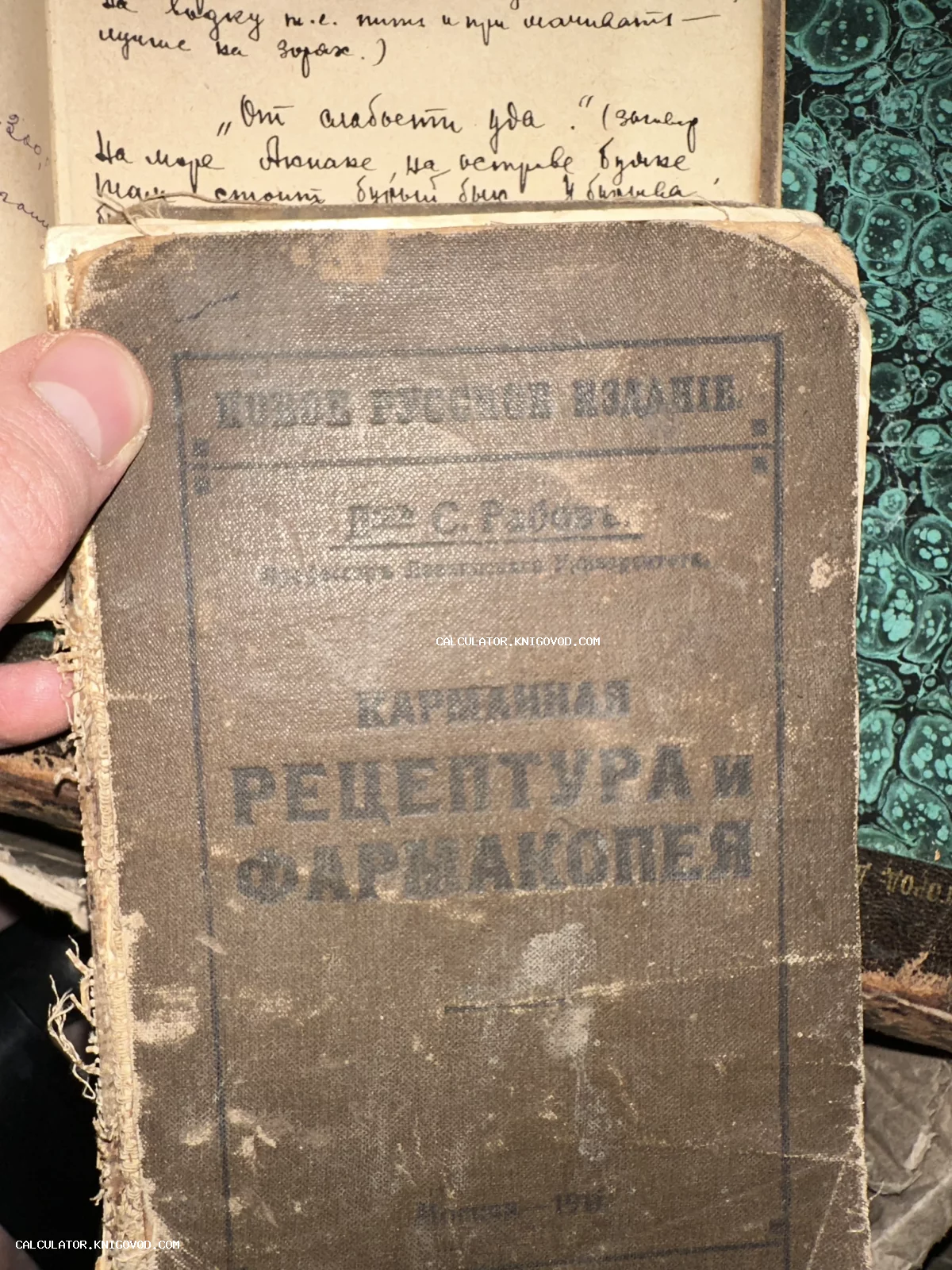 Старинная книга с потертой обложкой под названием 'Карманная рецептура и фармакопея' на фоне рукописных записей.