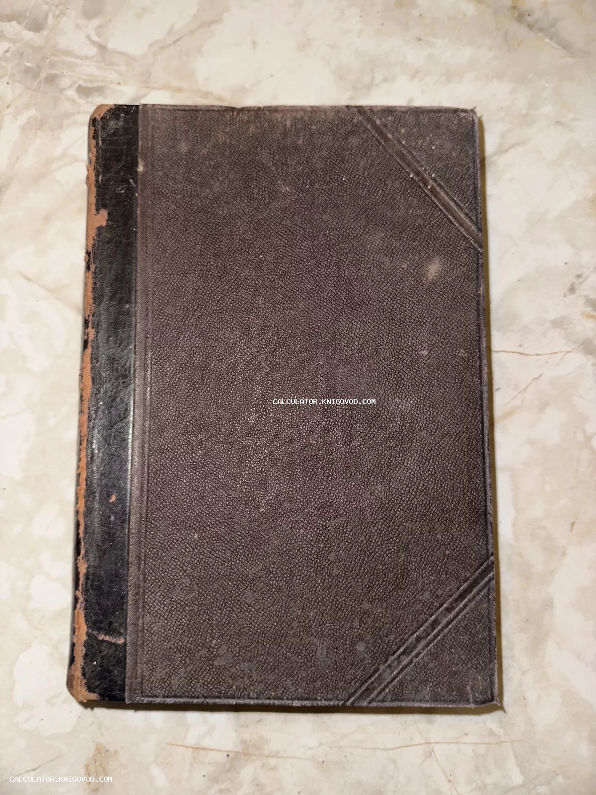 Старинная книга в темной обложке с зернистой текстурой и потертым корешком на светлом фоне.