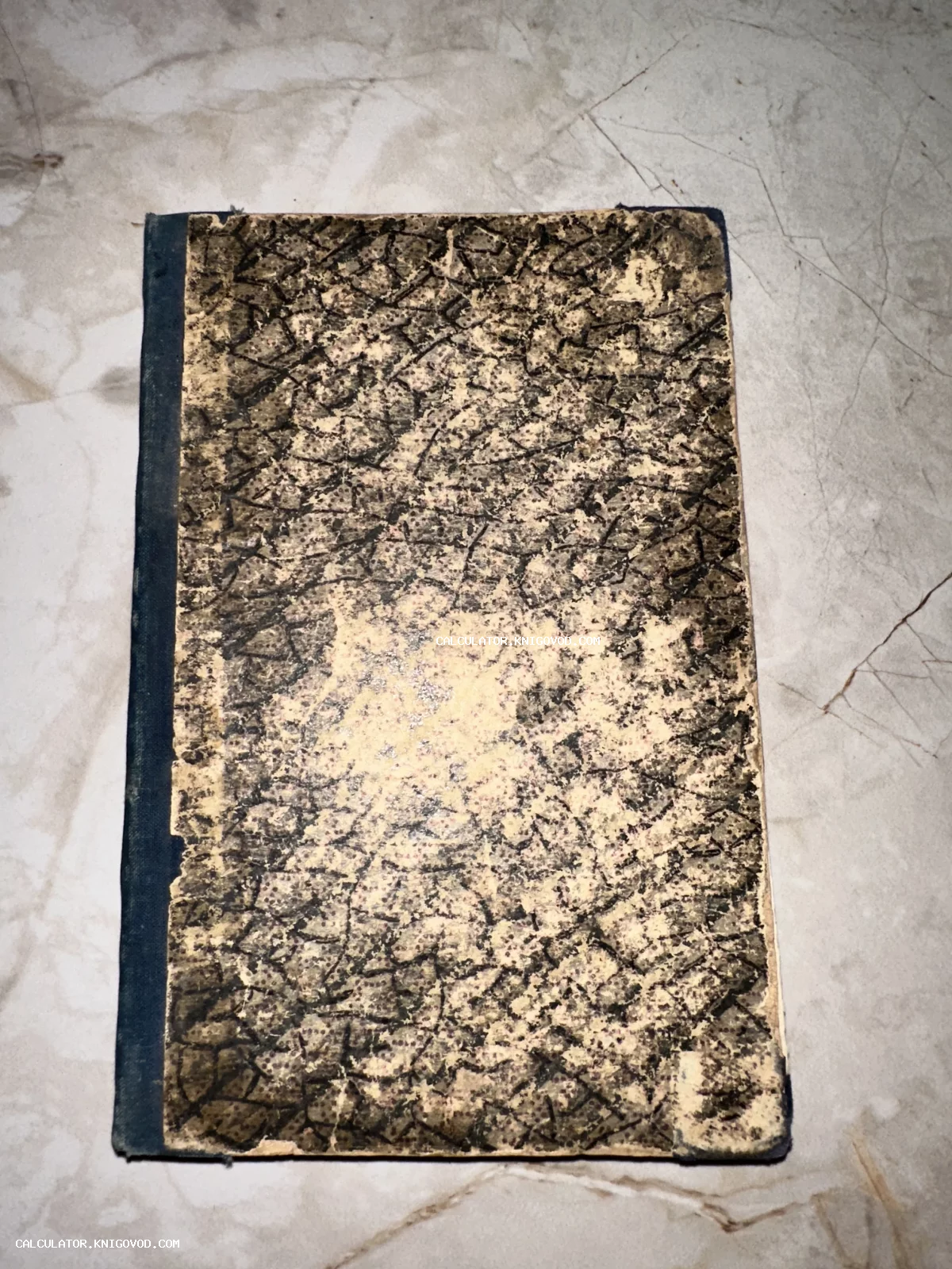 Старинная книга с характерным мраморным узором на обложке и синим тканевым корешком, вид сверху.
