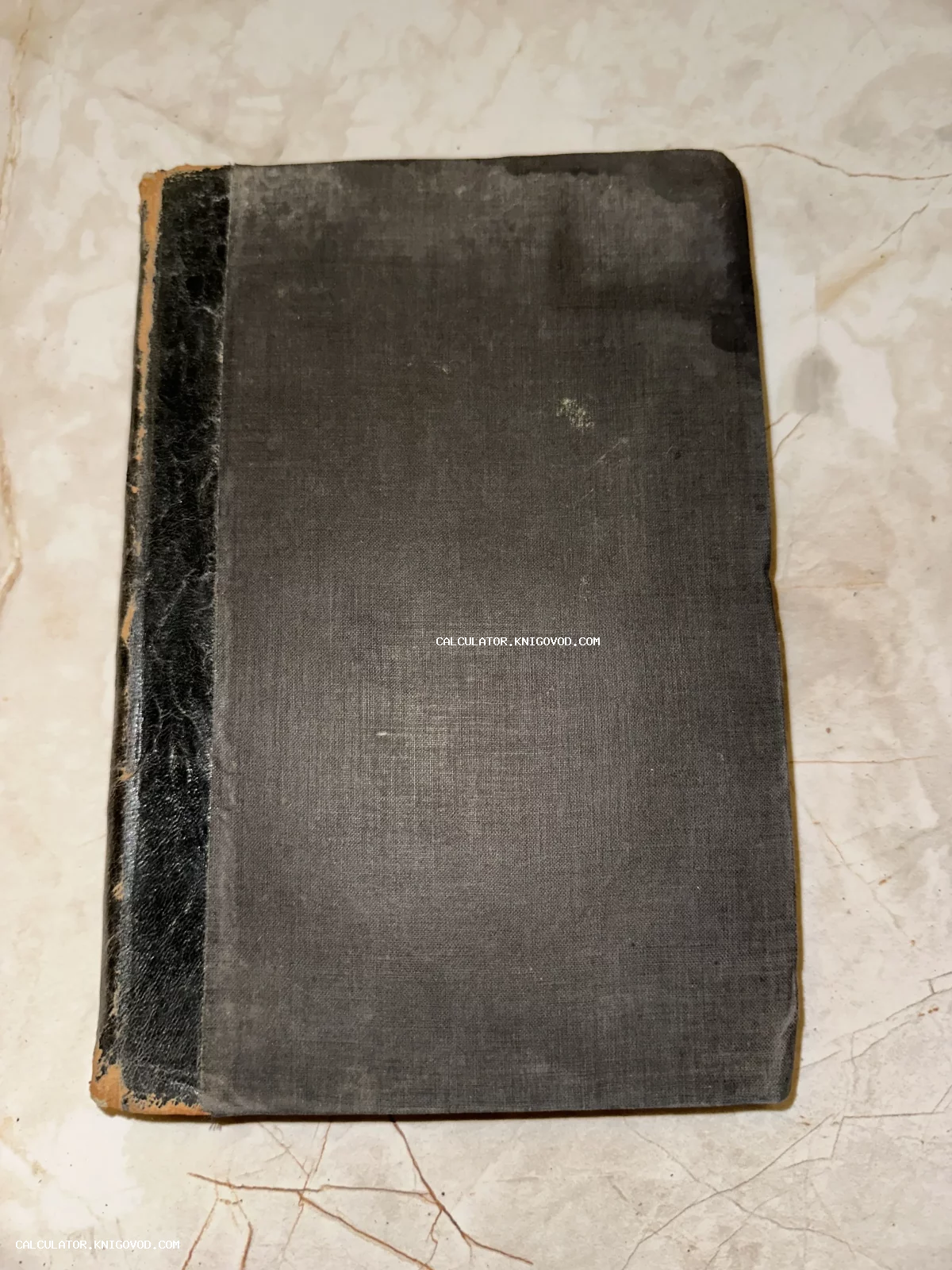 Старинная антикварная книга в темном тканевом переплете с черным кожаным корешком на мраморном фоне