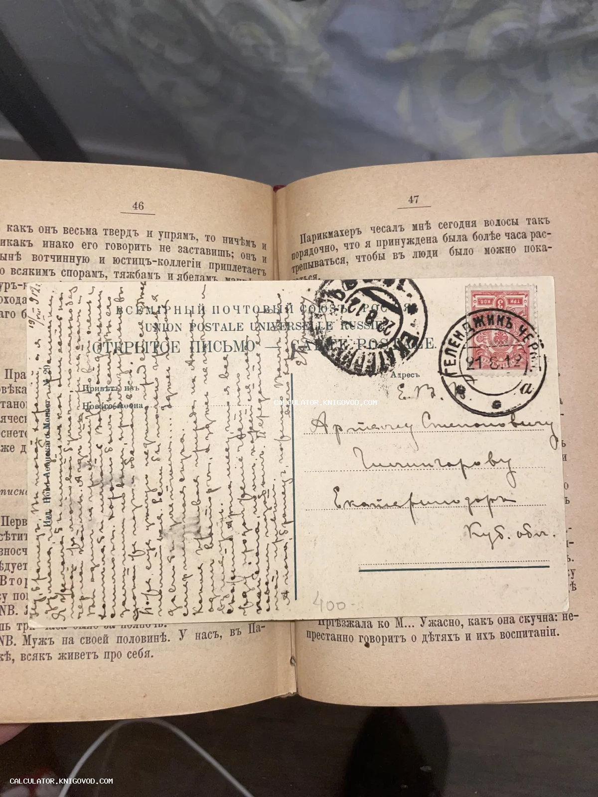 Антикварная почтовая открытка с рукописным текстом и почтовыми штемпелями начала XX века, лежащая на страницах старой книги.
