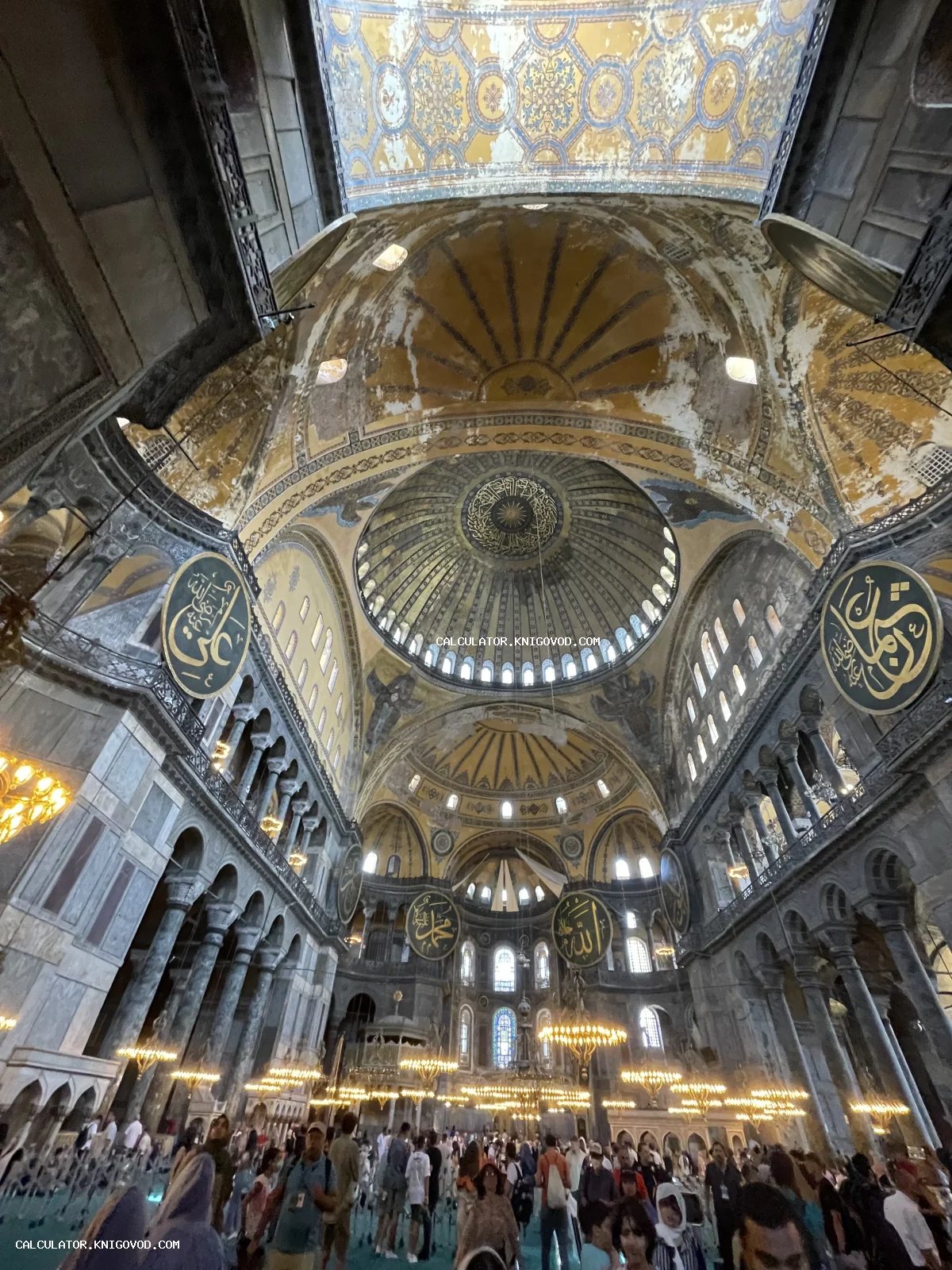 Интерьер собора Святой Софии с огромным центральным куполом, арабской каллиграфией на медальонах и множеством люстр.