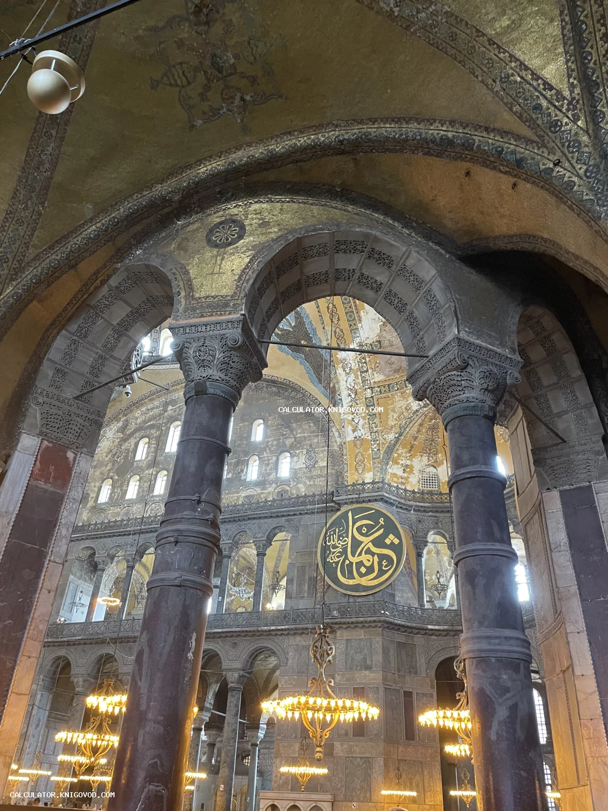 Величественный интерьер Айя-Софии с массивными колоннами, резными арками, золотыми византийскими мозаиками и круглым каллиграфическим медальоном.