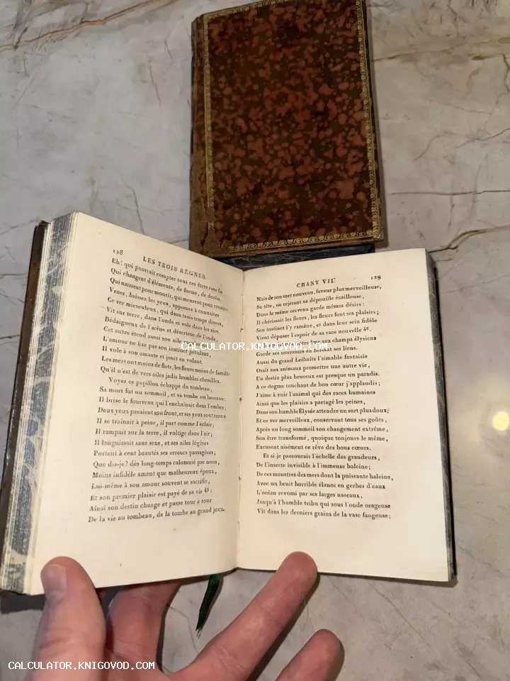 Раскрытая старинная книга на французском языке рядом с обложкой, украшенной мраморным узором и золотым тиснением.