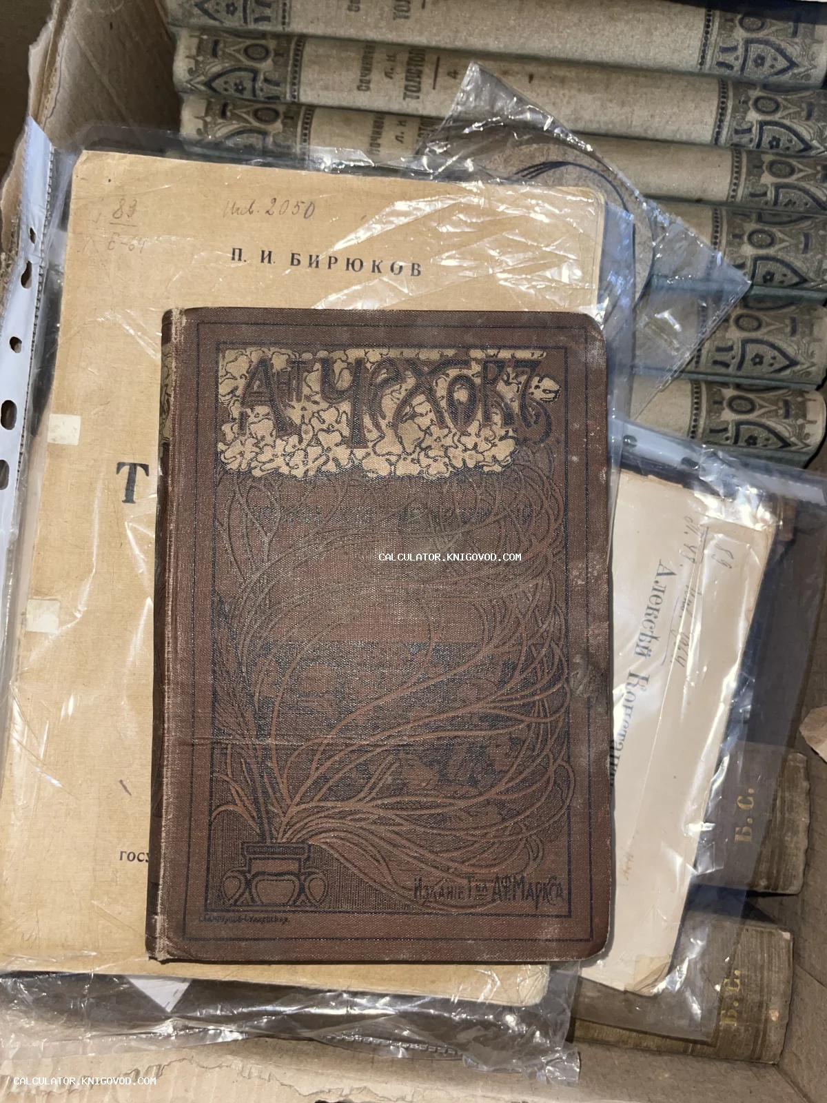 Старинная книга А. П. Чехова с декоративным растительным орнаментом на обложке, лежащая поверх архивных документов.