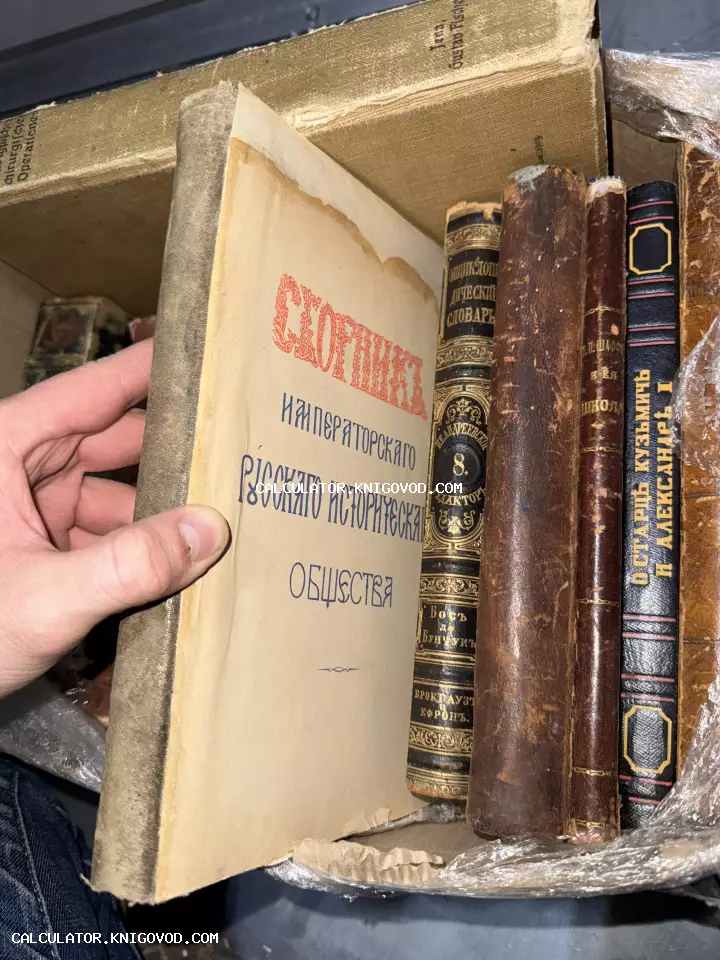 Рука открывает титульный лист старинной книги «Сборник Императорского Русского Исторического Общества» на фоне других антикварных книг в коробке.