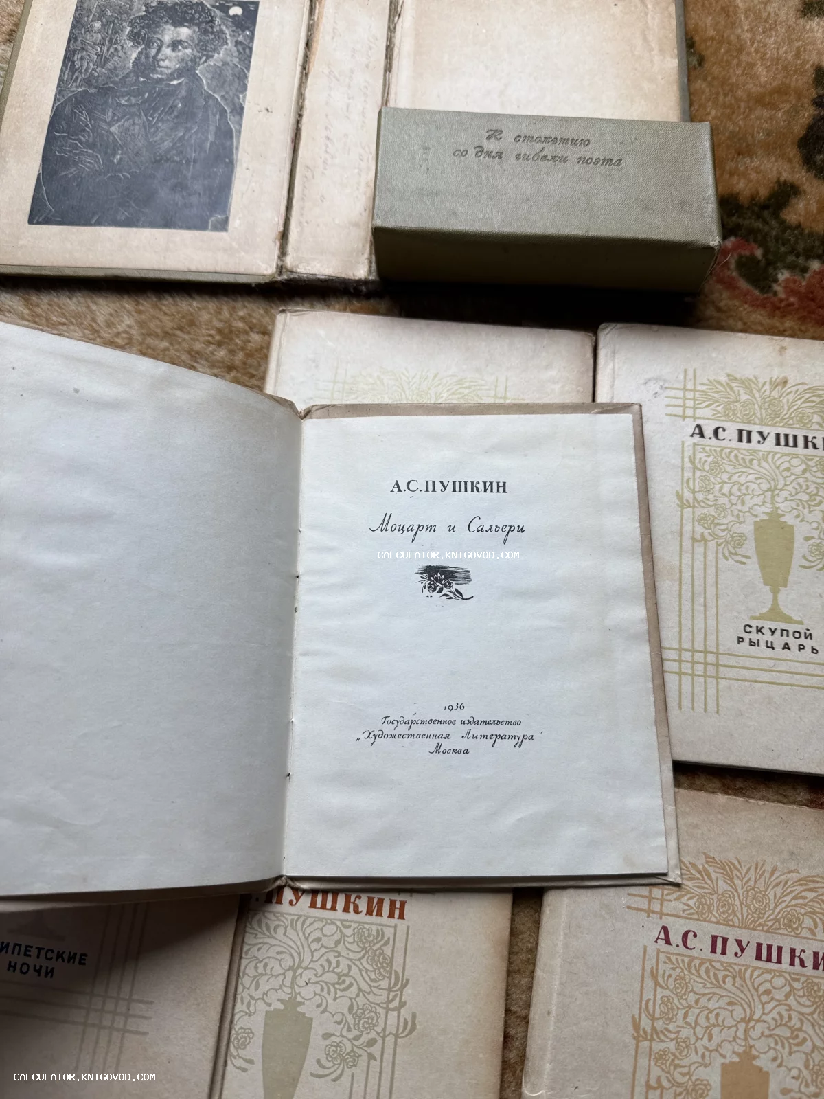 Раскрытая антикварная книга Пушкина «Моцарт и Сальери» на фоне портрета поэта и других томов серии в памятном футляре.