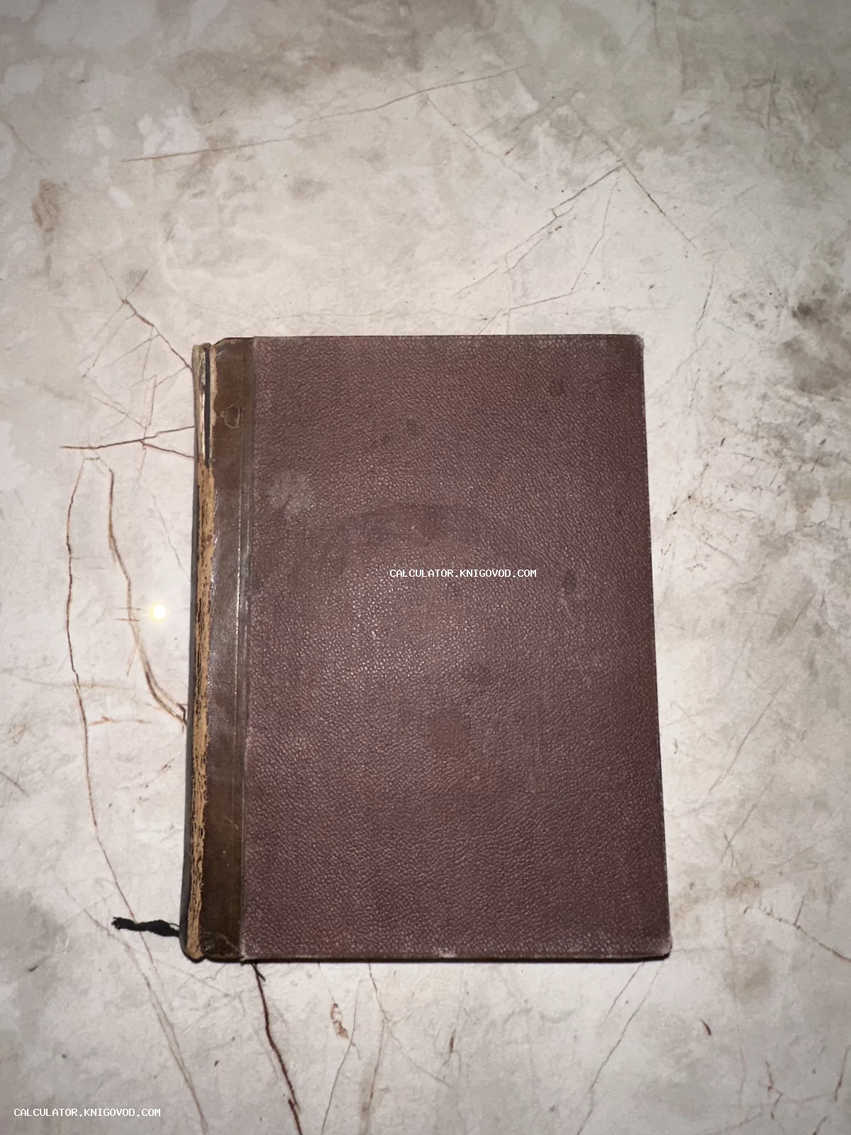 Вид сверху на антикварную книгу с потертым коричневым переплетом и кожаным корешком на мраморной поверхности.