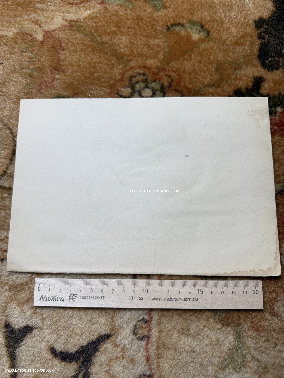 Оборотная сторона старинной фотографии или почтовой карточки на фоне ковра с измерительной линейкой