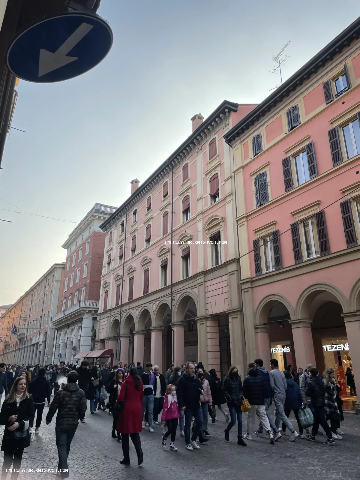 Вид на оживленную городскую улицу с классическими розовыми зданиями, украшенными арочными галереями и ставнями.