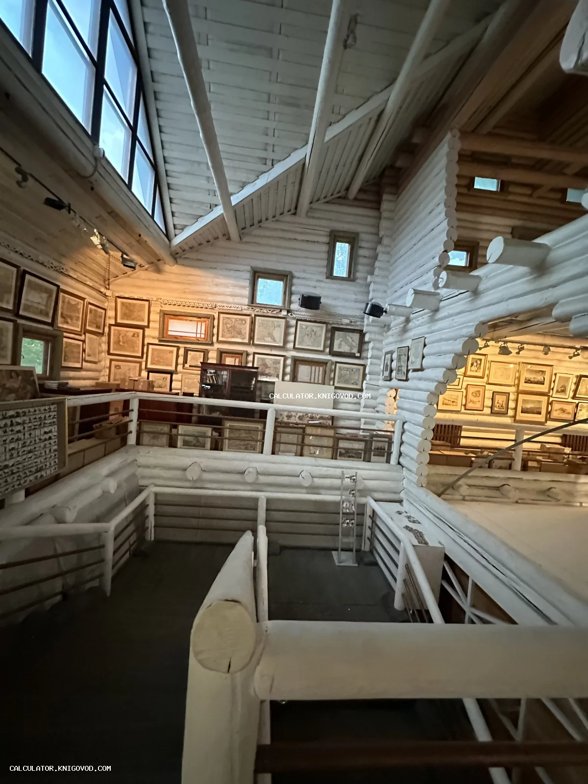 Просторный светлый интерьер бревенчатого дома, стены которого плотно декорированы старинными гравюрами и картами в рамках.