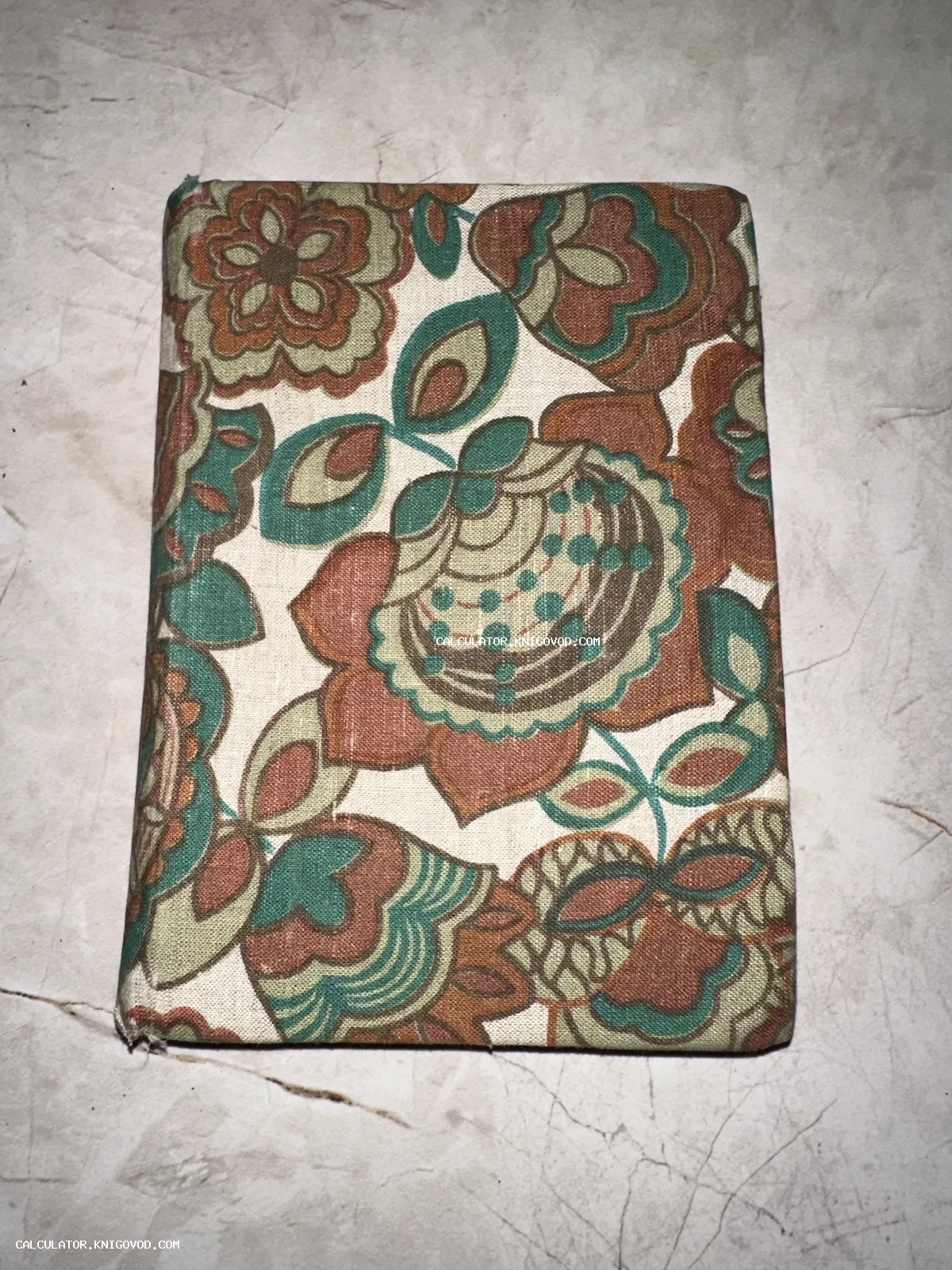 Старая книга в обложке из плотной ткани с крупным цветочным узором в коричневых и зеленых тонах.