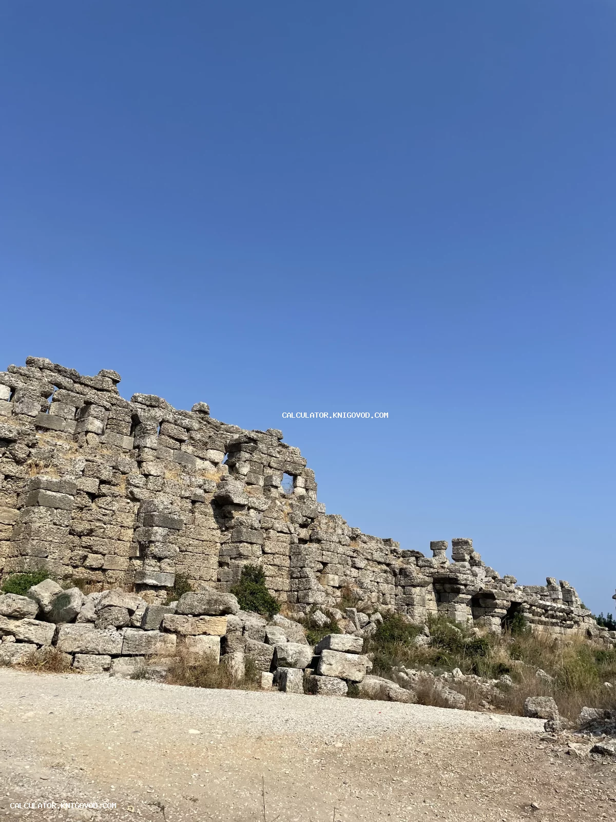 Вид на массивную стену из древних каменных блоков под ясным голубым небом.