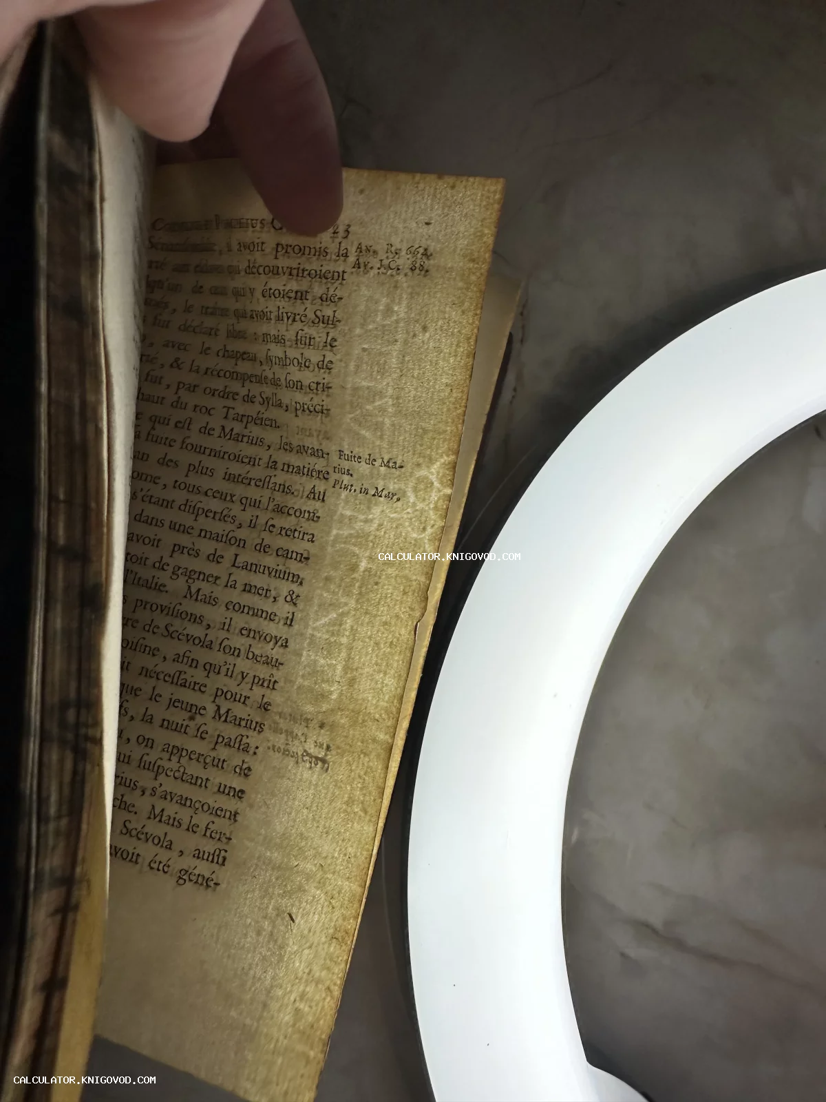 Крупный план пожелтевшей страницы старинной книги с текстом на французском языке и историческими комментариями на полях.