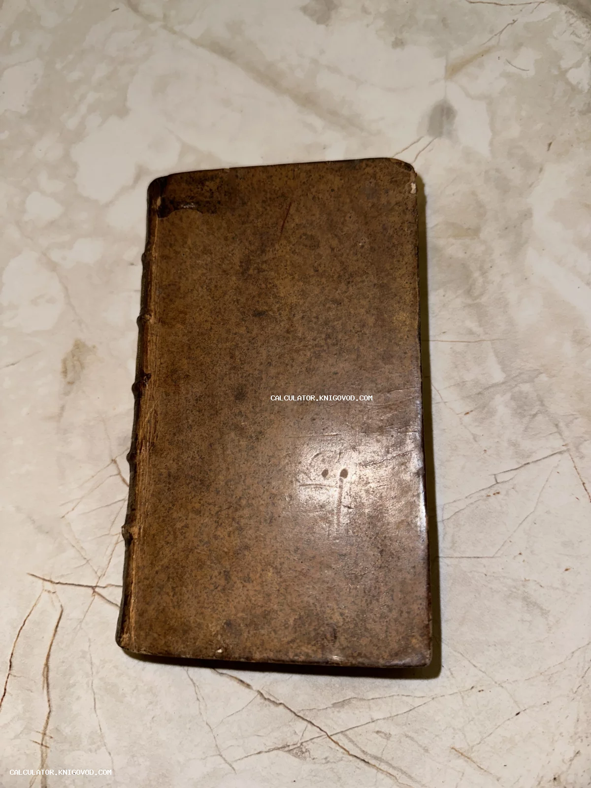 Антикварная книга в потертом коричневом кожаном переплете с бинтами на корешке на мраморном фоне.