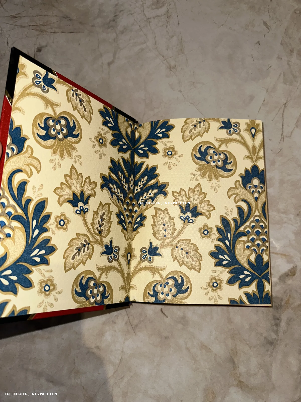 Раскрытая книга, демонстрирующая узорчатый форзац с сине-золотым цветочным рисунком на светлом фоне.