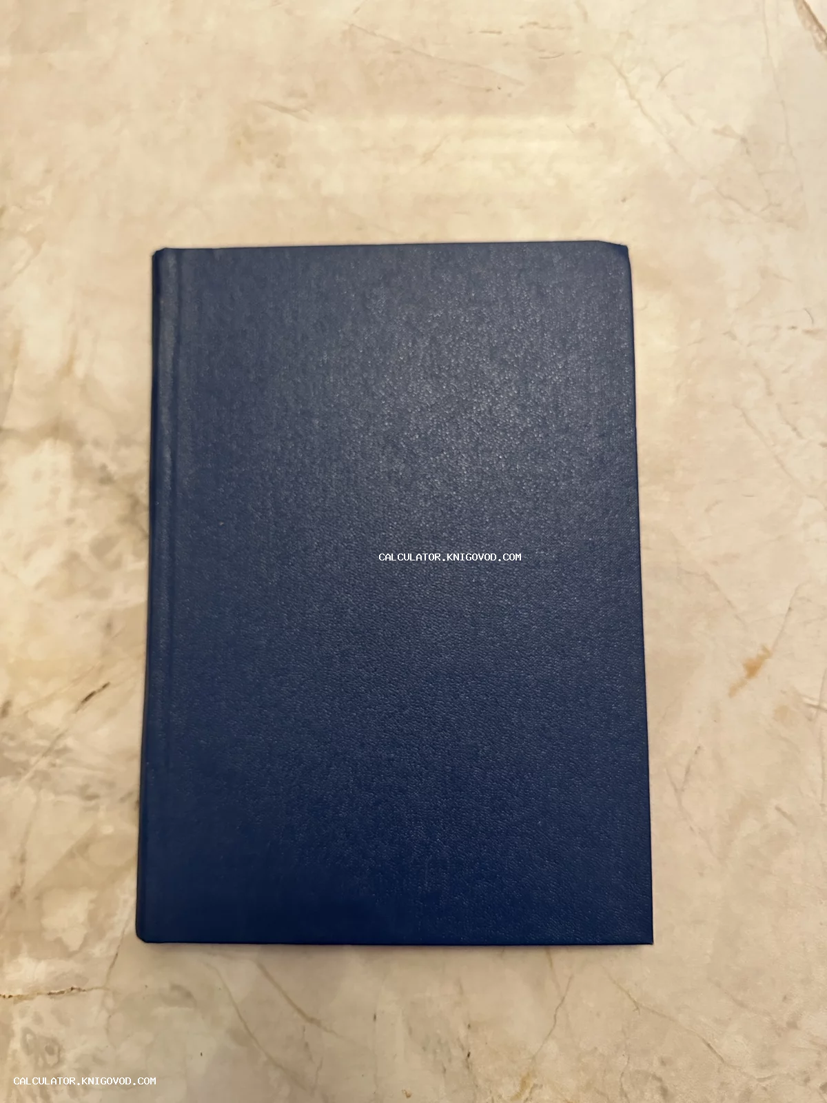 Синяя книга в твердом переплете с зернистой текстурой на мраморной поверхности.