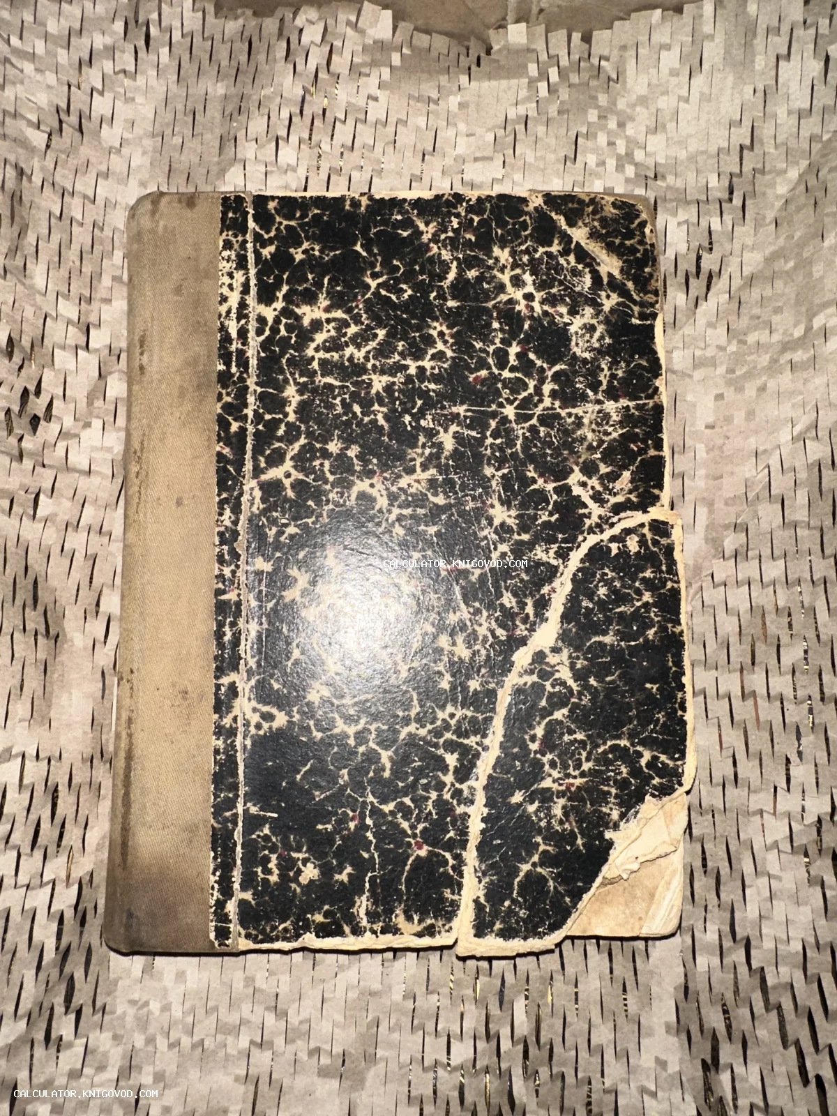 Антикварная книга с черно-белой мраморной обложкой и тканевым корешком, лежащая на упаковочном материале.