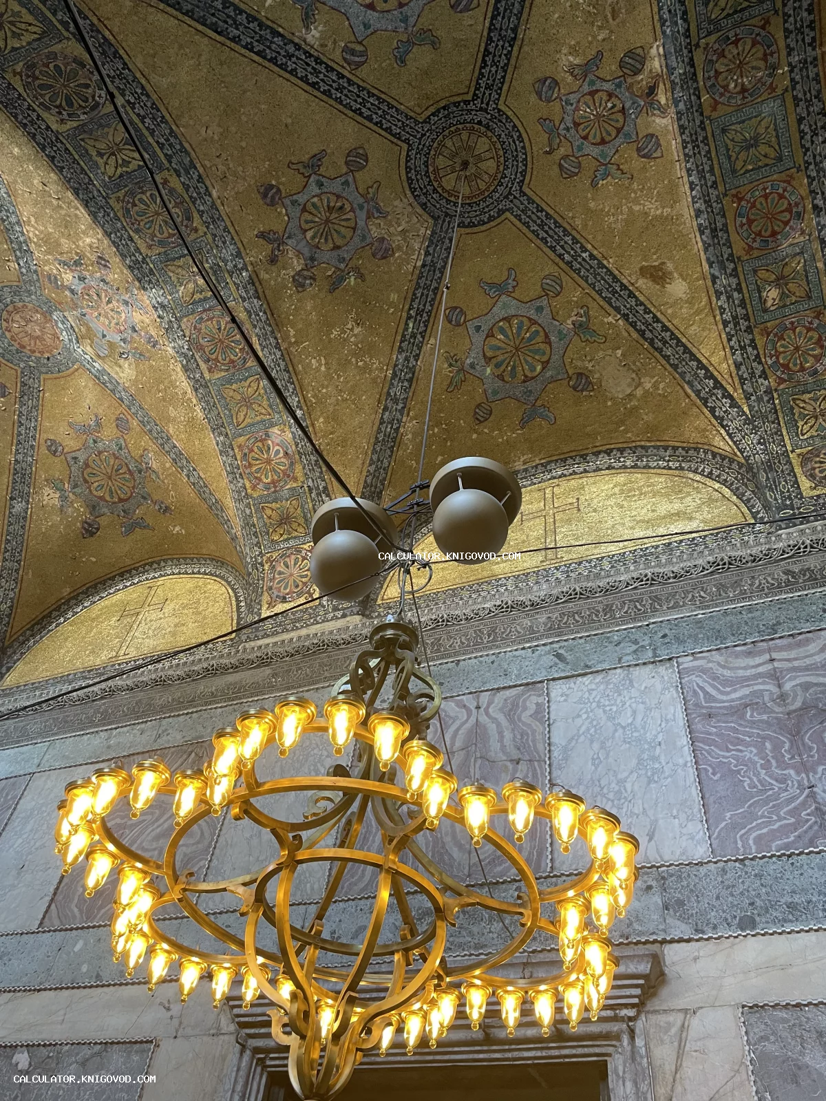 Интерьер древнего храма с золотыми мозаиками на потолке, мраморными стенами и большой круглой люстрой.