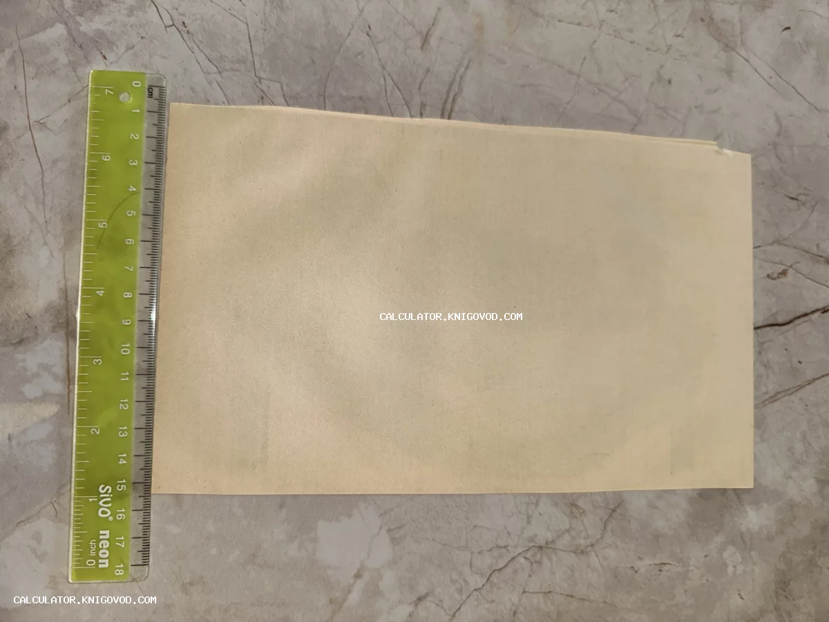 Старинный пожелтевший лист бумаги рядом с зеленой измерительной линейкой на мраморной поверхности.