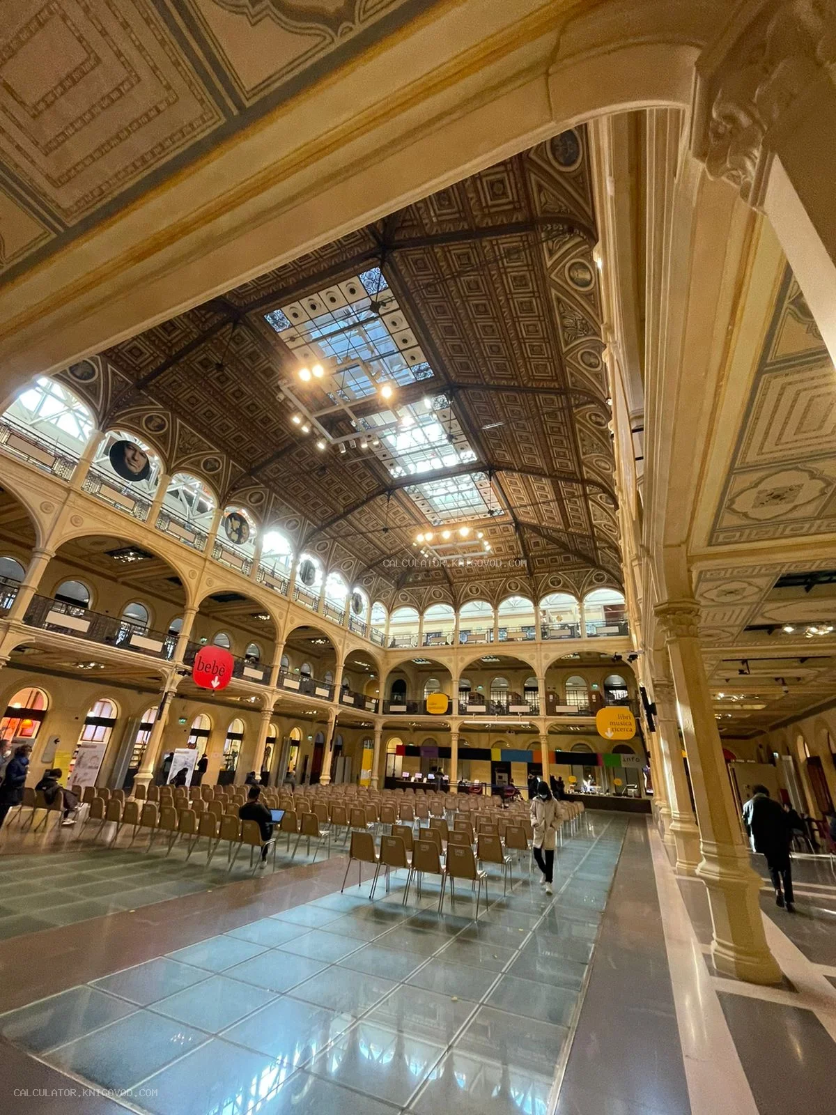 Интерьер просторного исторического зала с высоким декоративным кессонным потолком, многоуровневыми аркадами и рядами кресел.