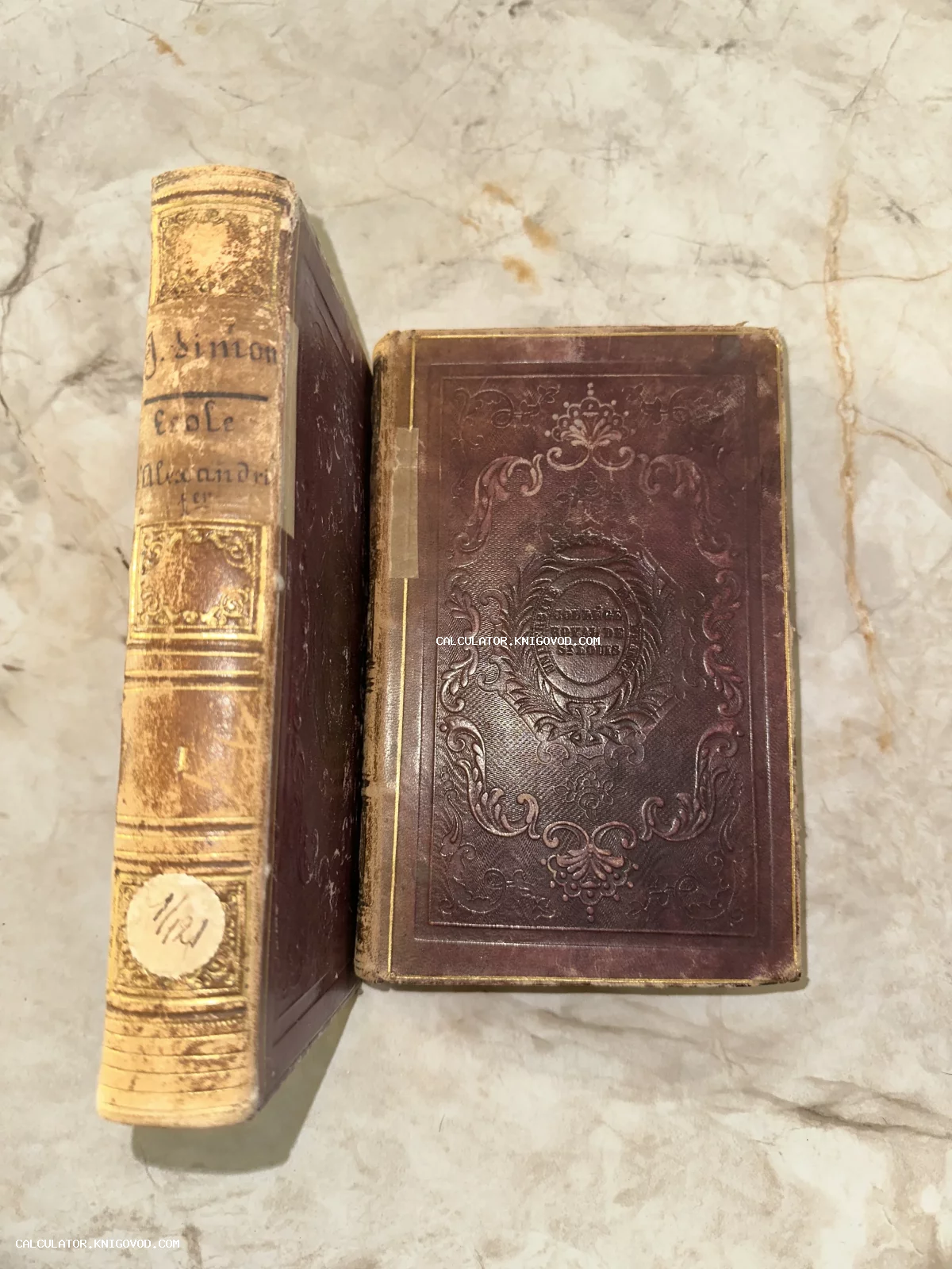 Старинная книга в бордовом кожаном переплете с золотым тиснением на корешке и декоративным орнаментом на обложке.