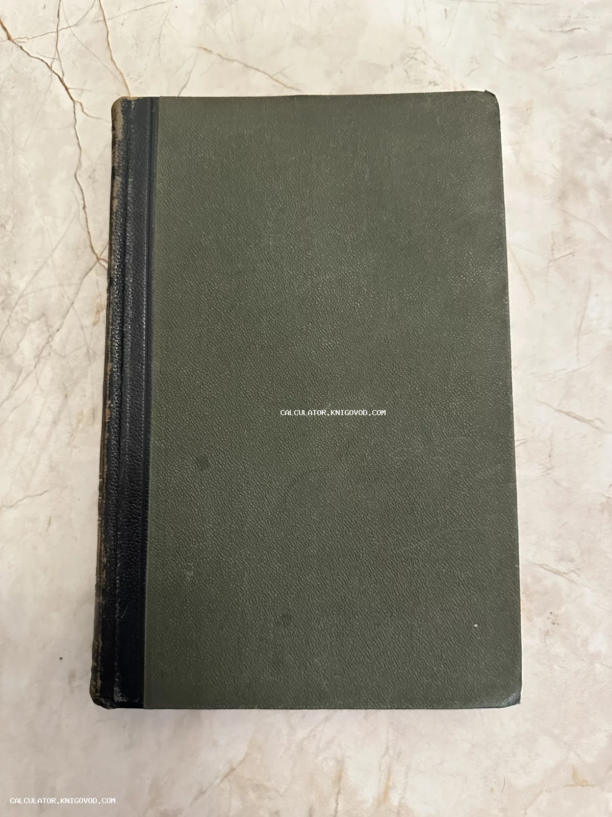 Старинная книга с темно-зеленой обложкой и черным корешком на светлом мраморном фоне