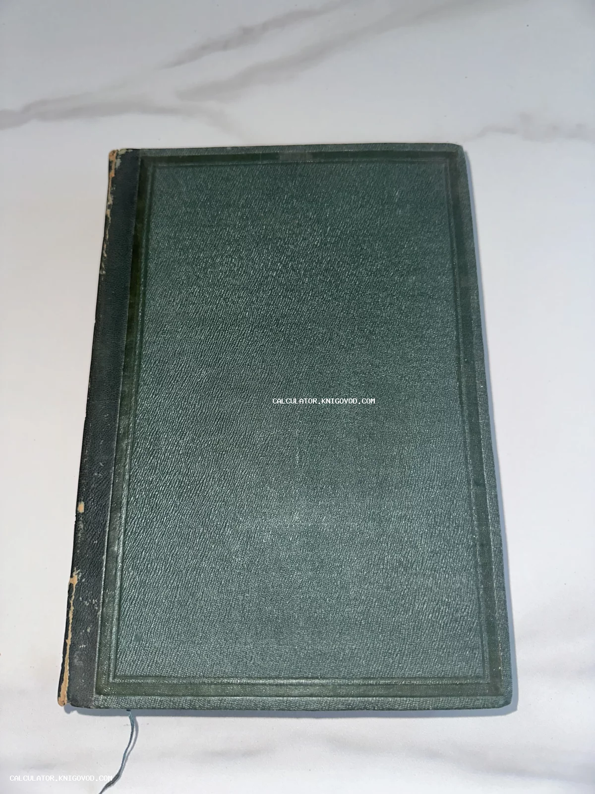 Вид сверху на старинную книгу в темно-зеленом тканевом переплете с тиснением и потертым корешком.