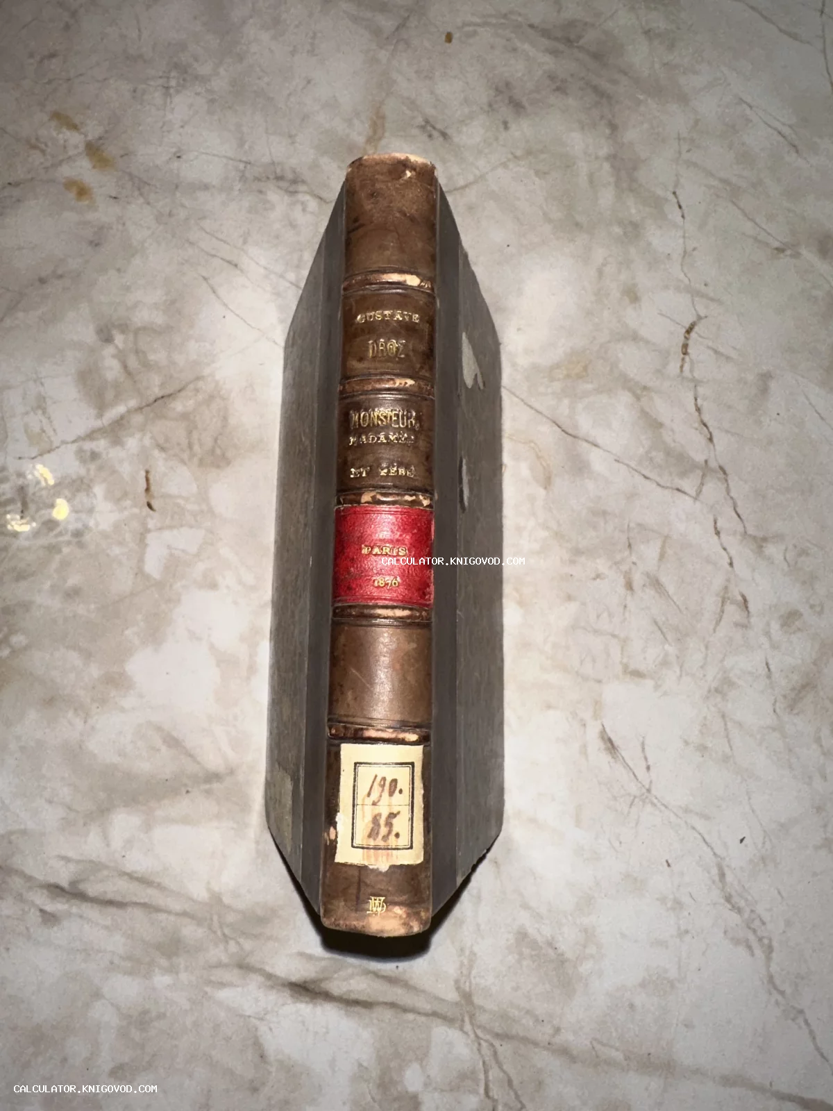 Корешок антикварной книги Гюстава Дро Monsieur, Madame et Bébé в кожаном переплете с золотым тиснением на мраморном столе.