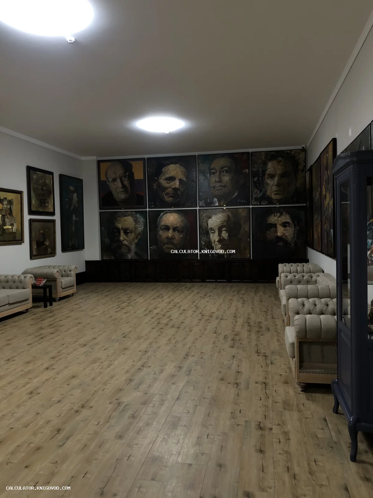 Интерьер просторного зала с экспозицией масштабных портретов на стенах и рядами бежевых стеганых кресел.