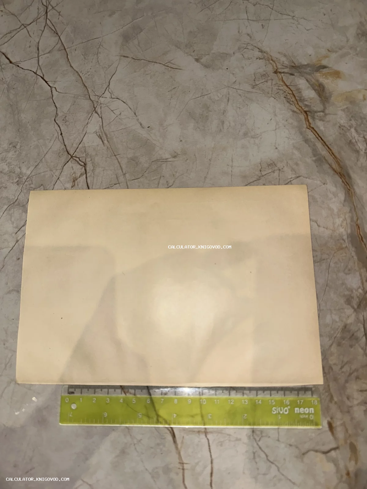 Пожелтевший прямоугольный лист старой бумаги рядом с зеленой прозрачной линейкой на мраморном столе.