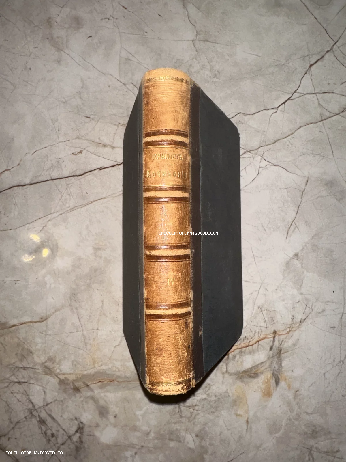 Корешок антикварной книги в кожаном переплете с золотым тиснением и надписью «Крыловъ Сочиненія IV» на мраморном фоне.