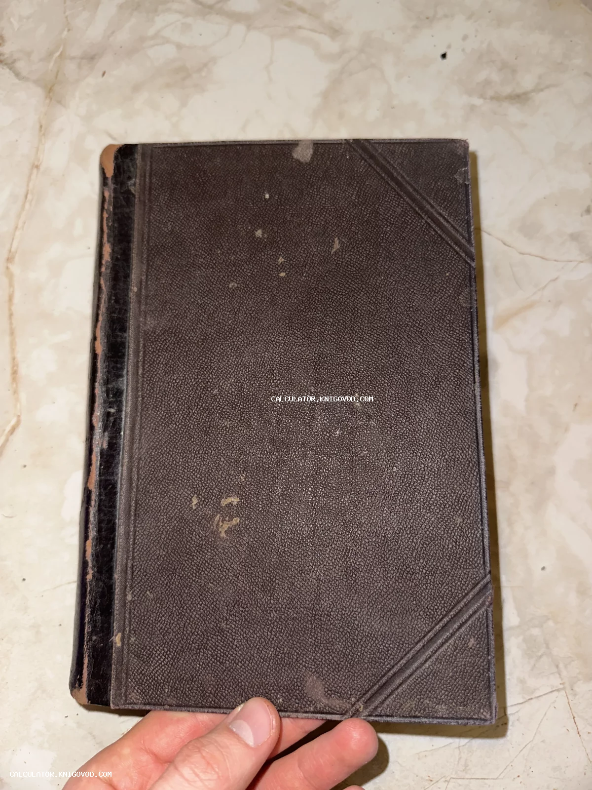 Крупный план обложки старинной книги темно-коричневого цвета с потертостями и линейным тиснением по углам.