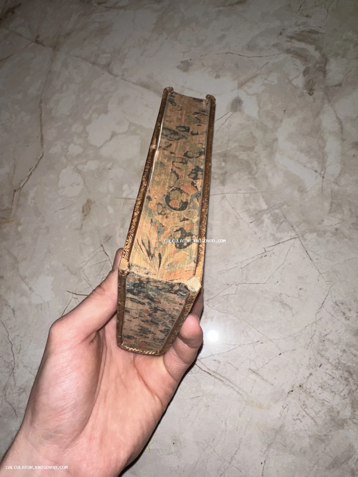 Вид сверху на старинную книгу с мраморным узором на обложке, которую держат в руке