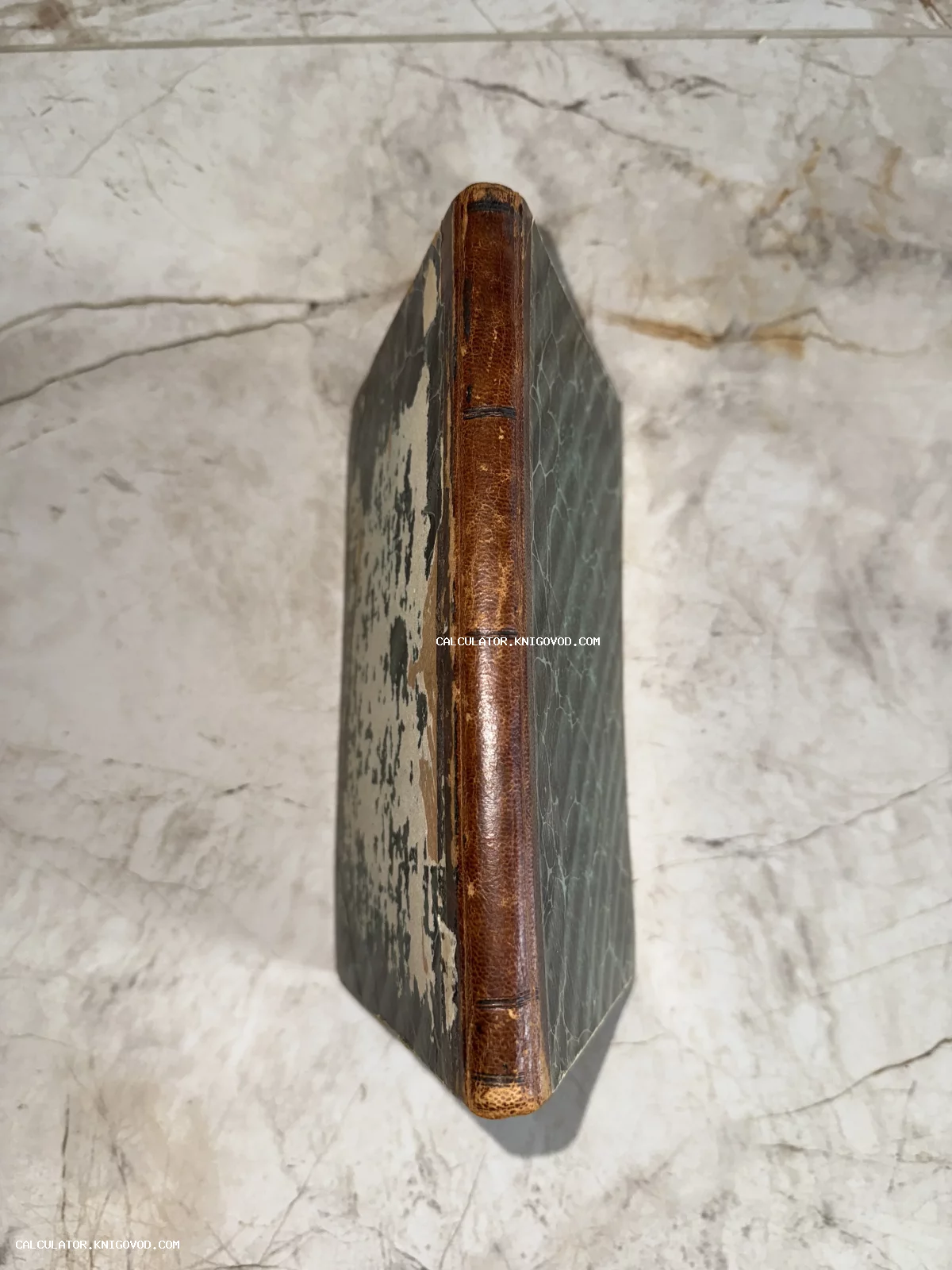 Вид сверху на корешок старинной книги в коричневом кожаном переплете с потертыми крышками из мраморной бумаги.