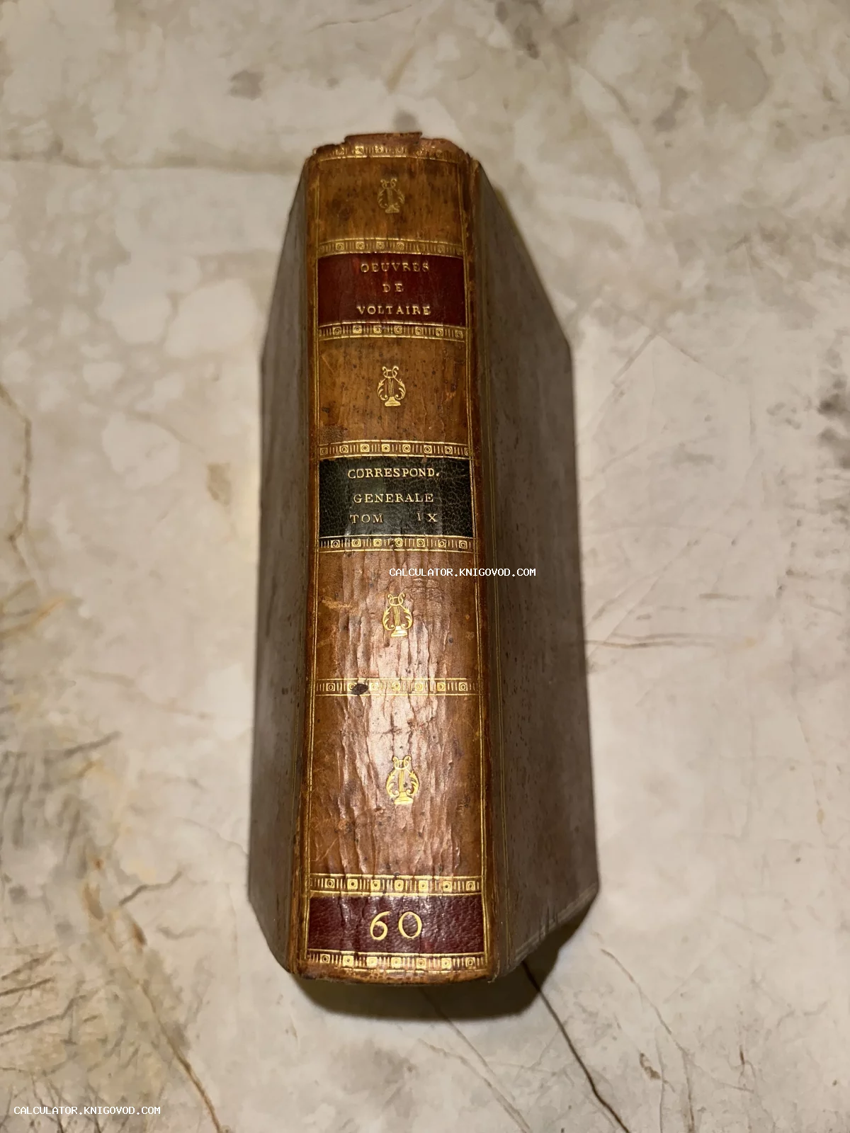 Корешок антикварной книги Вольтера с золотым тиснением и изображением лир на коричневой коже.